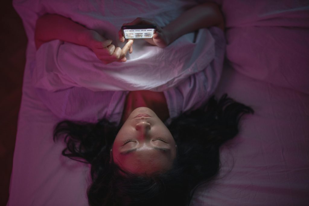 pexels-photo-7351144-7351144 A woman lying in bed at night browsing her smartphone under soft lighting.